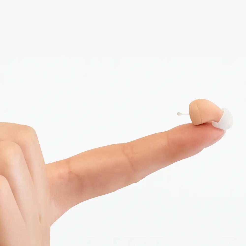 One Future Hearing Comfort hearing aid balanced on a fingertip, smaller than the fingernail