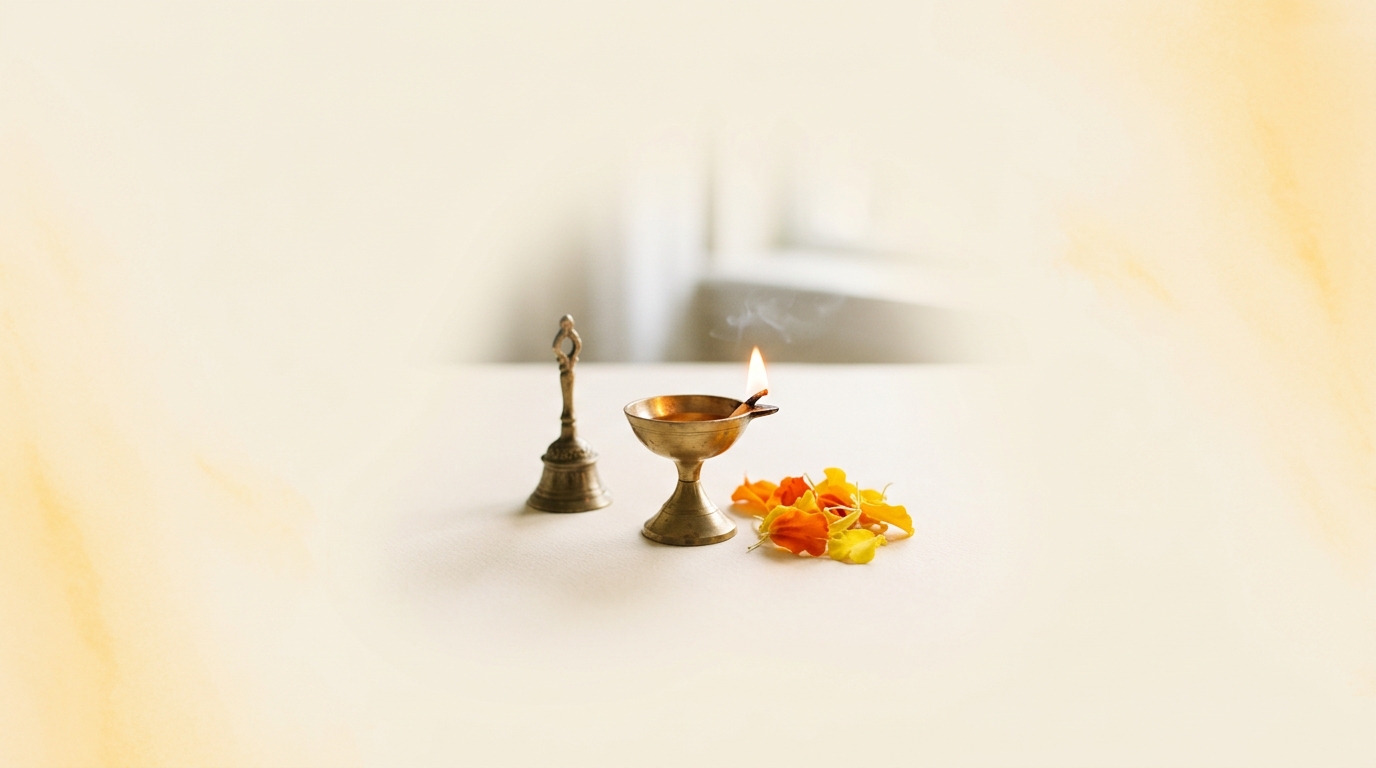 A lit brass diya, bell, and marigold petals