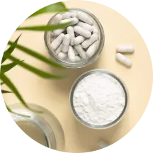 Glass jars containing white capsules and powder on a beige surface with a green plant nearby.