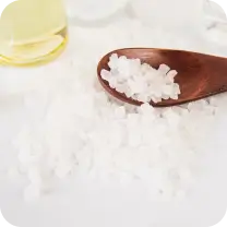 Wooden spoon with coarse salt next to a glass container of liquid.