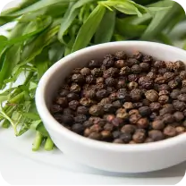 Bowl of black peppercorns with fresh greens in the background.