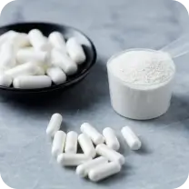 White capsules and a scoop of white powder on a gray surface.