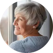 Elderly woman with short hair smiling while looking out a window.