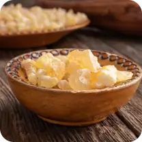 A wooden bowl filled with frankincense resin pieces on a rustic wooden surface.