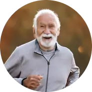 Elderly man with white beard jogging outdoors and smiling.