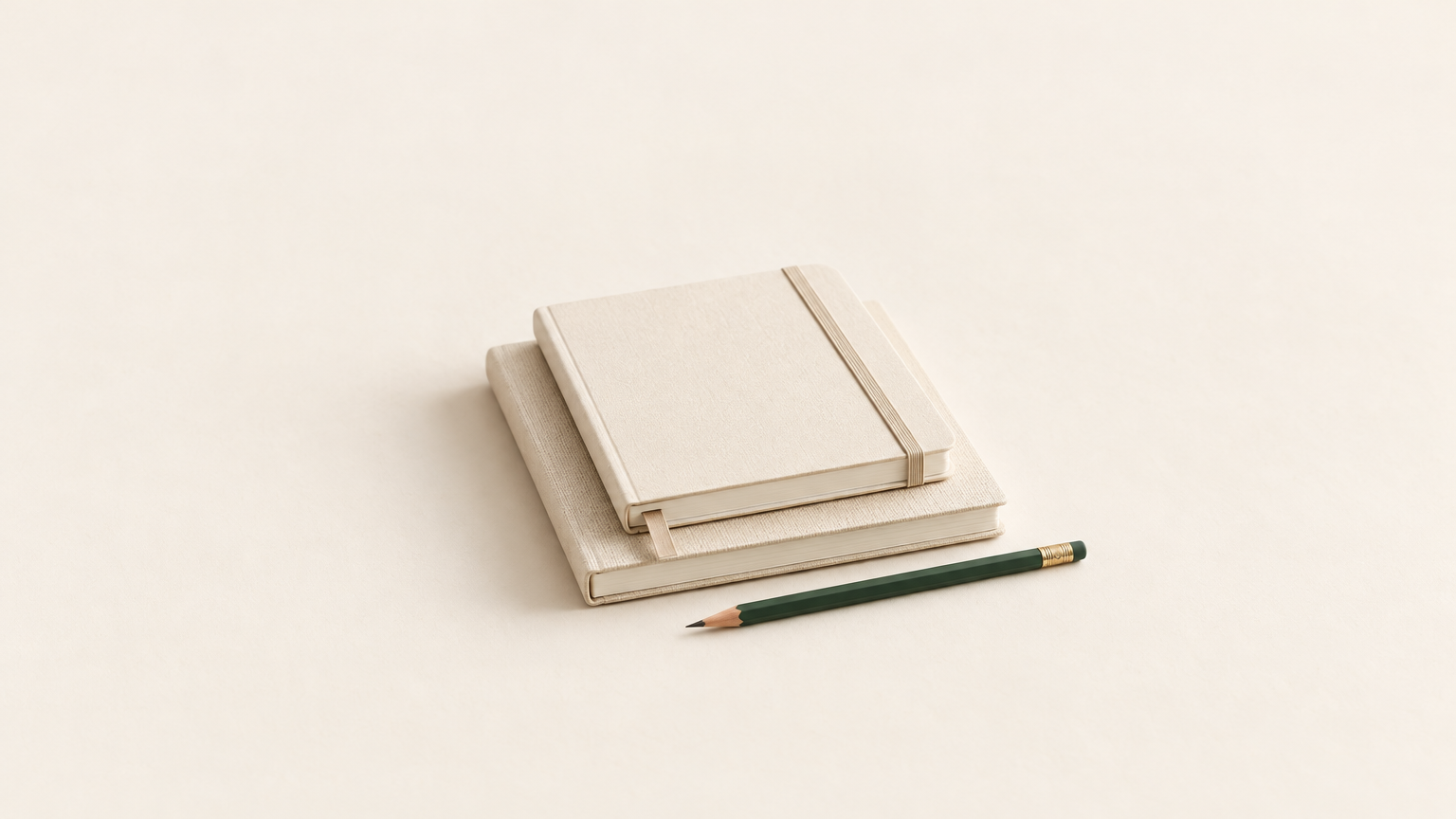 A stack of cream notebooks and a forest-green pencil