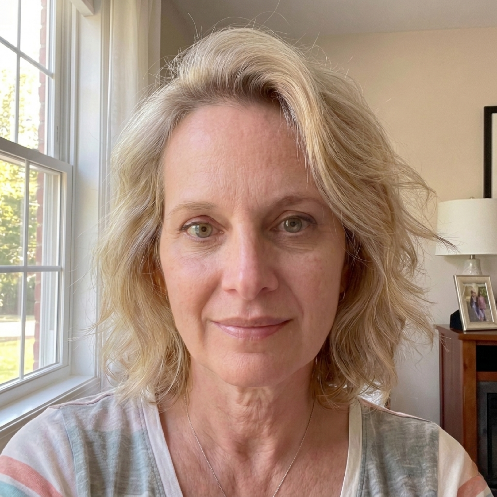 A woman with shoulder-length wavy blonde hair and green eyes looks at the camera.