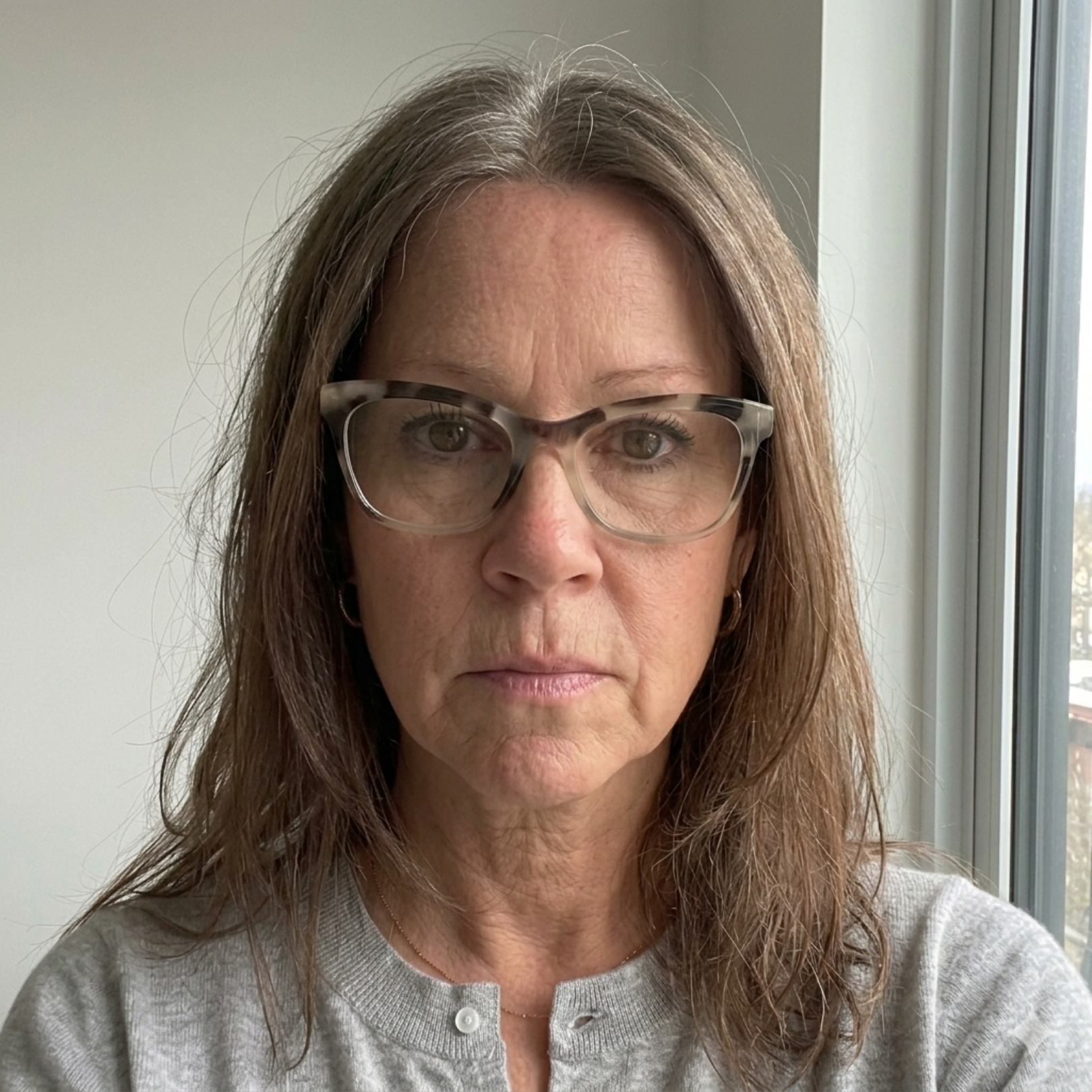 A headshot of a woman with long, brown and grey hair, wearing glasses and a grey cardigan.