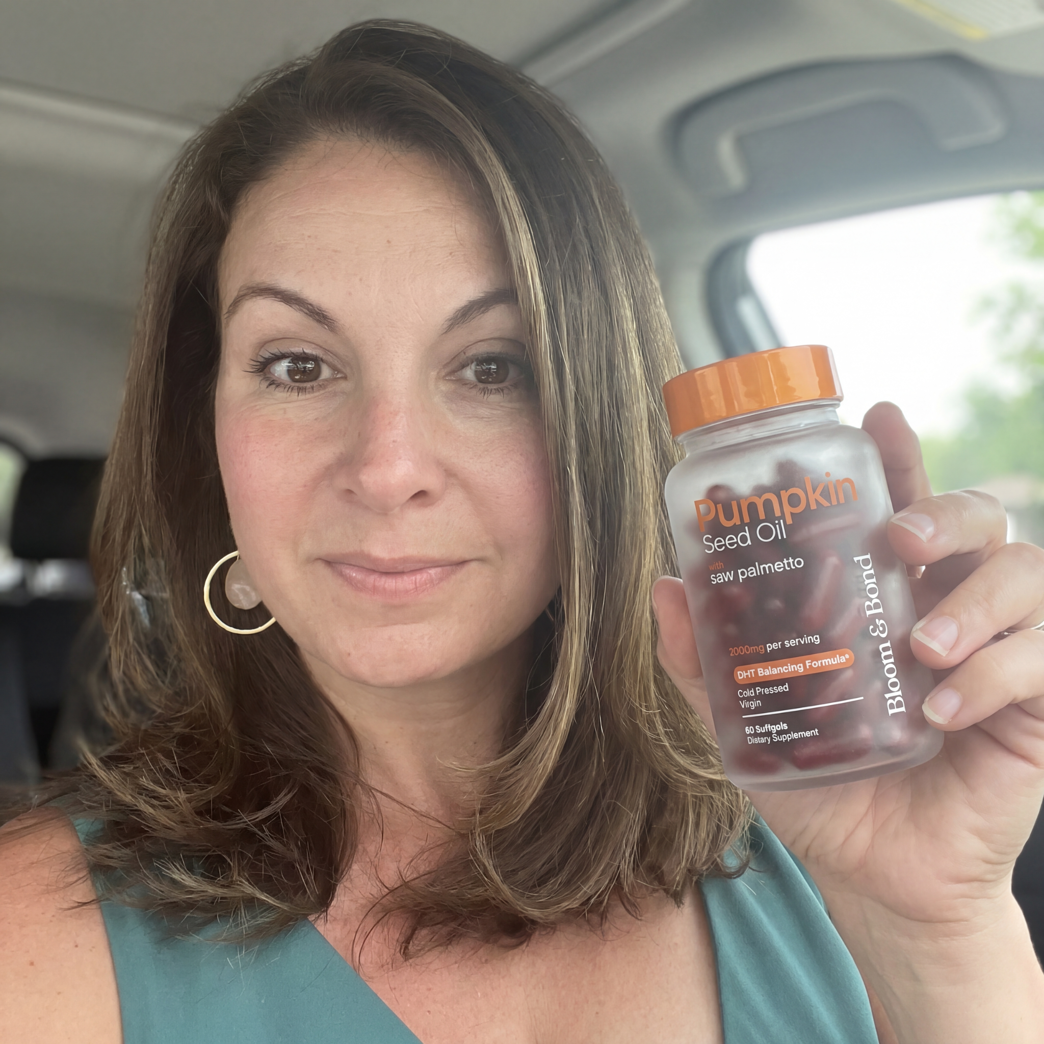 A woman sits in her car holding a bottle of Bloom & Bond Pumpkin Seed Oil supplements.