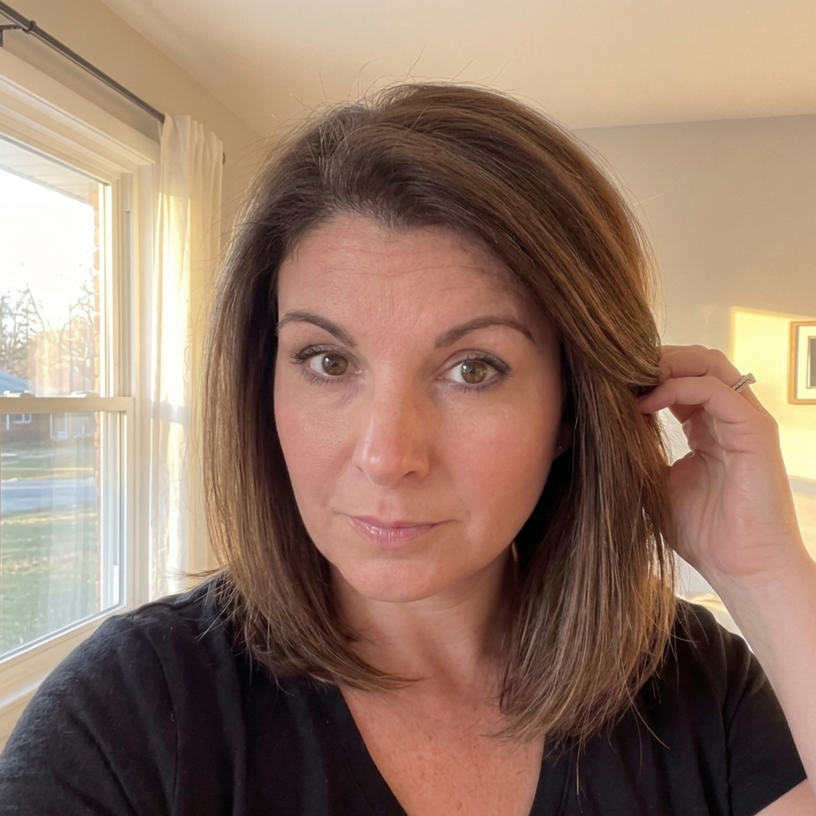 A woman with shoulder-length brown hair looking at the camera, with her hand in her hair.
