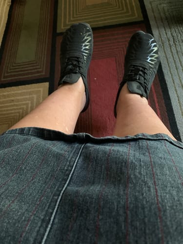 Reviewer's black Lorax Pro barefoot shoes worn on feet while sitting on a patterned rug.
