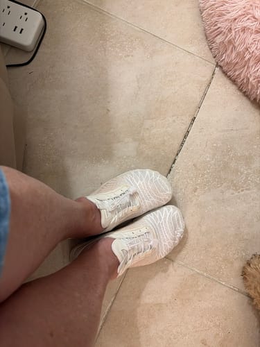 Reviewer's white Lorax Pro barefoot shoes on feet while standing on a tiled floor.