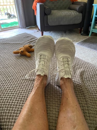 Customer relaxing with their feet up, showing their white Lorax Pro barefoot shoes in a living room.