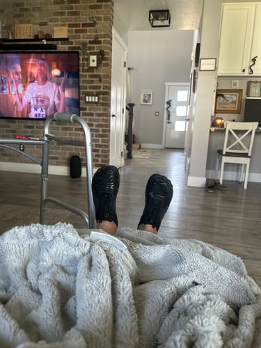 Customer relaxing at home with their feet up, showing the soles of their black Lorax Pro barefoot shoes.