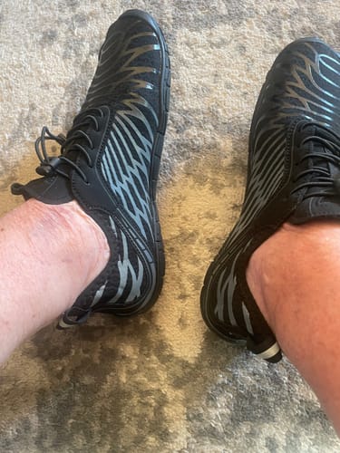 Reviewer's black Lorax Pro barefoot shoes with pattern worn on feet over a textured carpet.