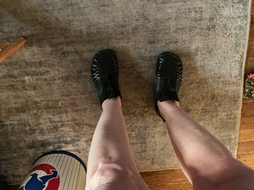 Customer's overhead view of their new, black Lorax Pro barefoot shoes being worn on a rug.