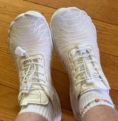 A customer's top-down view of their feet in white Lorax Pro barefoot shoes with socks on a wooden floor.
