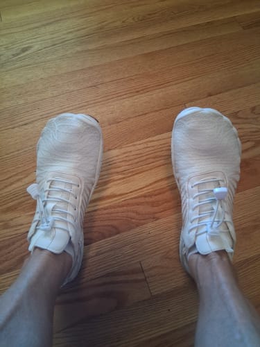 Customer's white Lorax Pro barefoot shoes worn on feet, viewed from above while standing on a wooden floor.