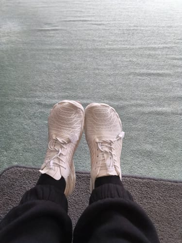 Reviewer's perspective looking down at their white Lorax Pro barefoot shoes, worn with black pants.