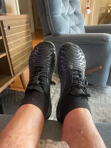 Customer's Lorax Pro barefoot shoes in black with a dark patterned design, worn on feet while relaxing.