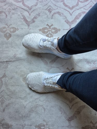Customer's feet wearing white Lorax Pro barefoot shoes on a patterned rug.