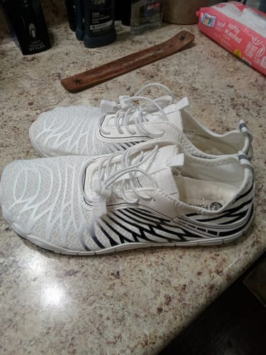 Customer's pair of white Lorax Pro barefoot shoes with black striped patterns resting on a speckled countertop.