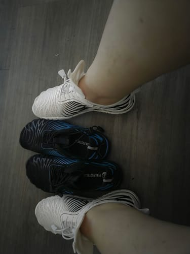 Customer's Lorax Pro barefoot shoes, with a person wearing white pairs and holding black pairs on a floor.