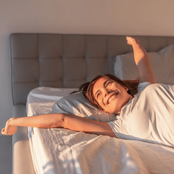 Woman smiling and stretching in bed during the morning sunlight.
