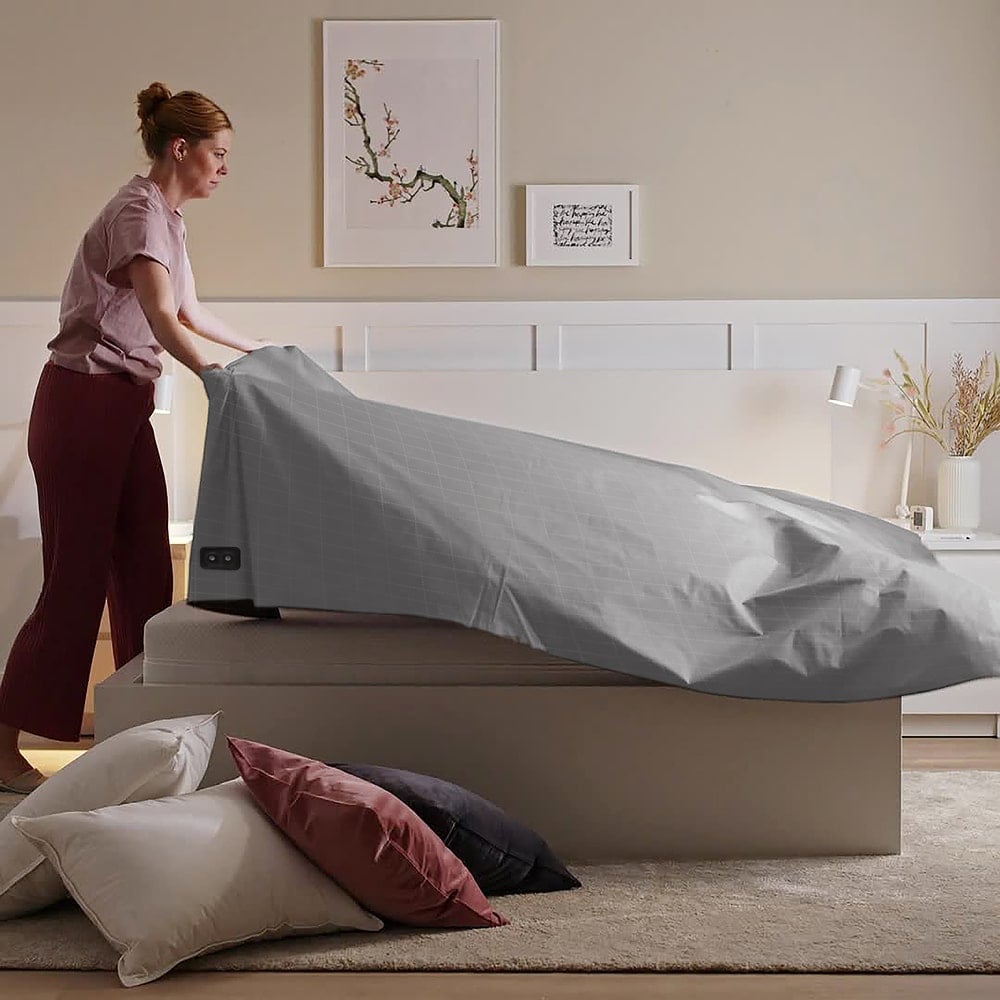 A woman adjusting a gray bedspread in a neatly decorated bedroom.