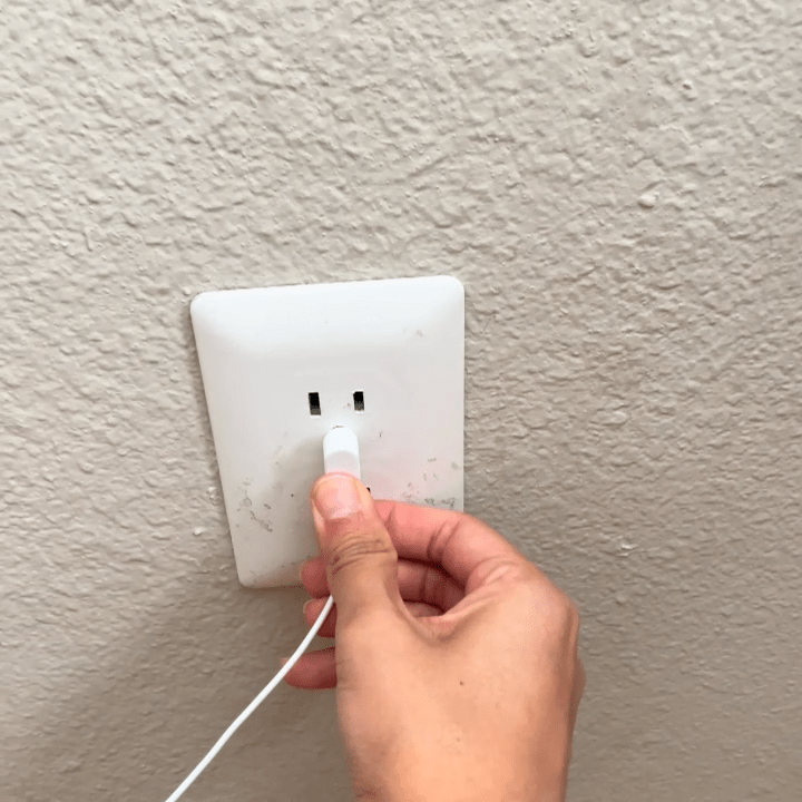 Hand plugging a charger into a wall socket.