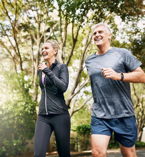 A man and a woman jogging together in a park, smiling and enjoying the outdoors.