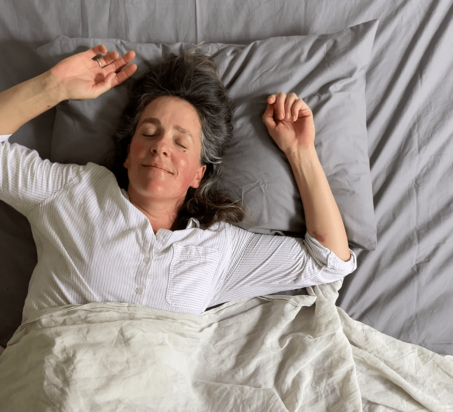 A person in white pajamas lies comfortably in bed with a content expression.